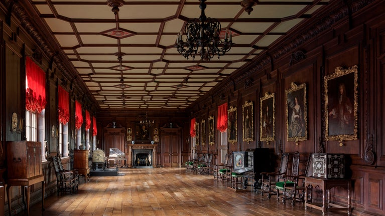 The Long Gallery at Chirk Castle with portraits on the walls and cabinets next to the walls
